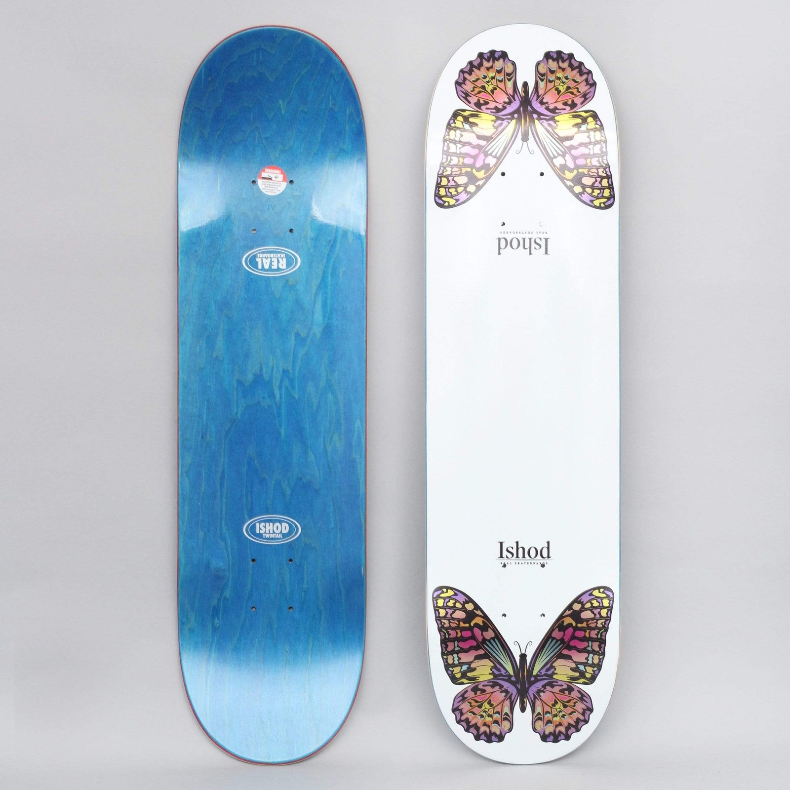 Real Ishod Monarch TT White skateboard deck: White deck with a pair of colourful monarch butterflies in pink, yellow and purple, one at each end, with 'Ishod' in small serif type between them. The photo also shows the blue-stained underside.