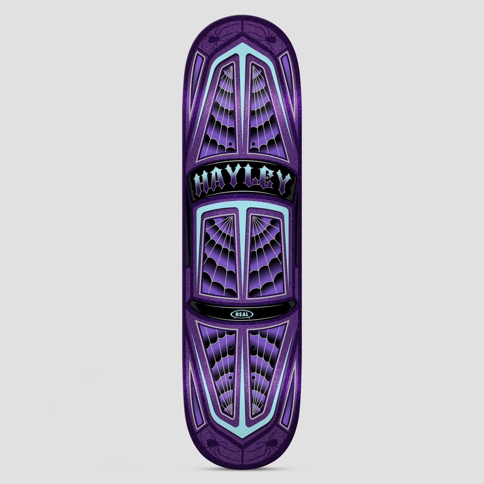 Real Hayley Threadline True Fit skateboard deck: Top-down view of a lowrider-style car body in purple glitter, with spider-web patterns in the windows and pale turquoise trim. A black plaque in the centre carries gothic lettering, and small spiders sit at both ends.