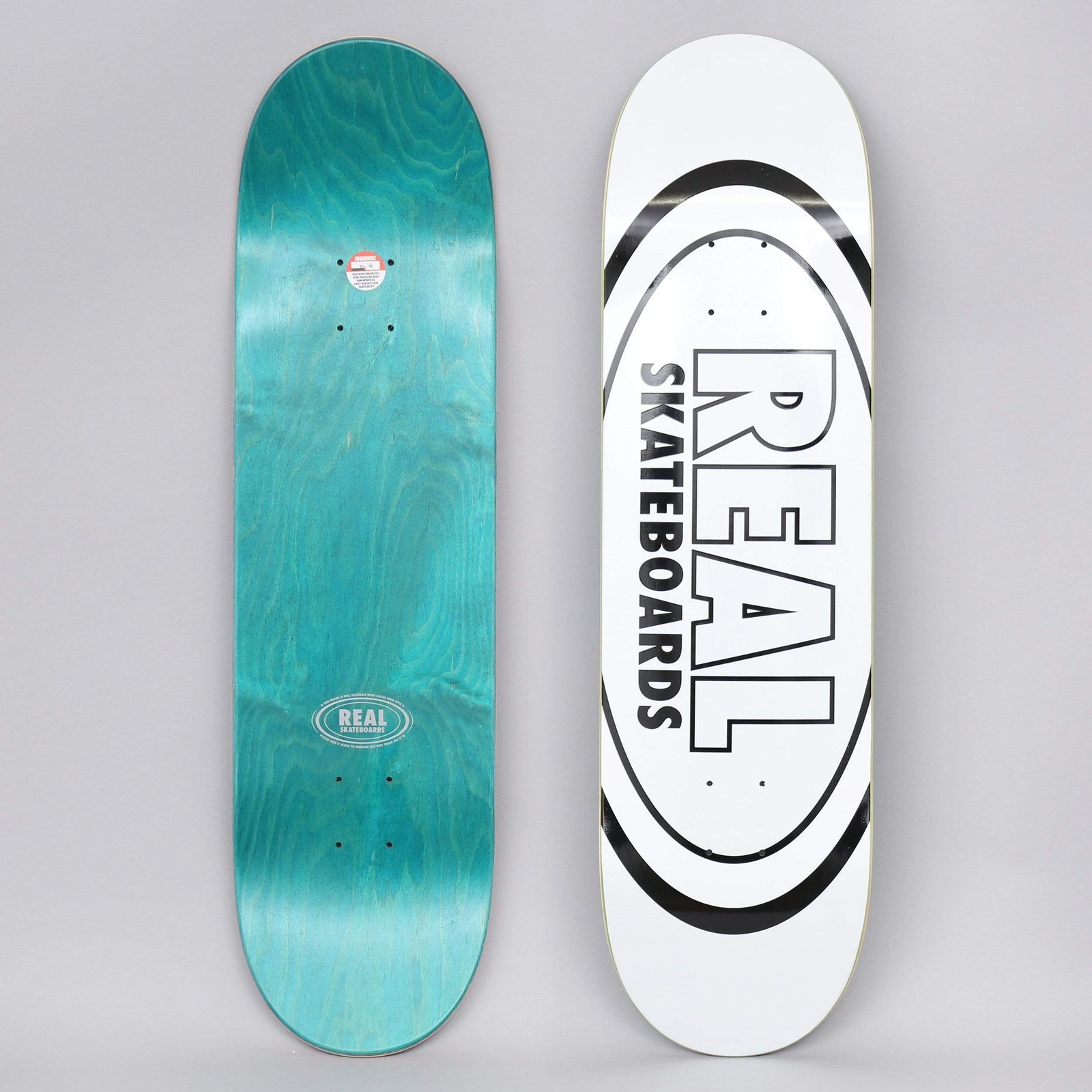 Real Classic Oval White skateboard deck: White deck with the Real logo, REAL SKATEBOARDS in black outlined block letters inside a large black oval. The photo also shows the teal underside with a small Real oval logo.