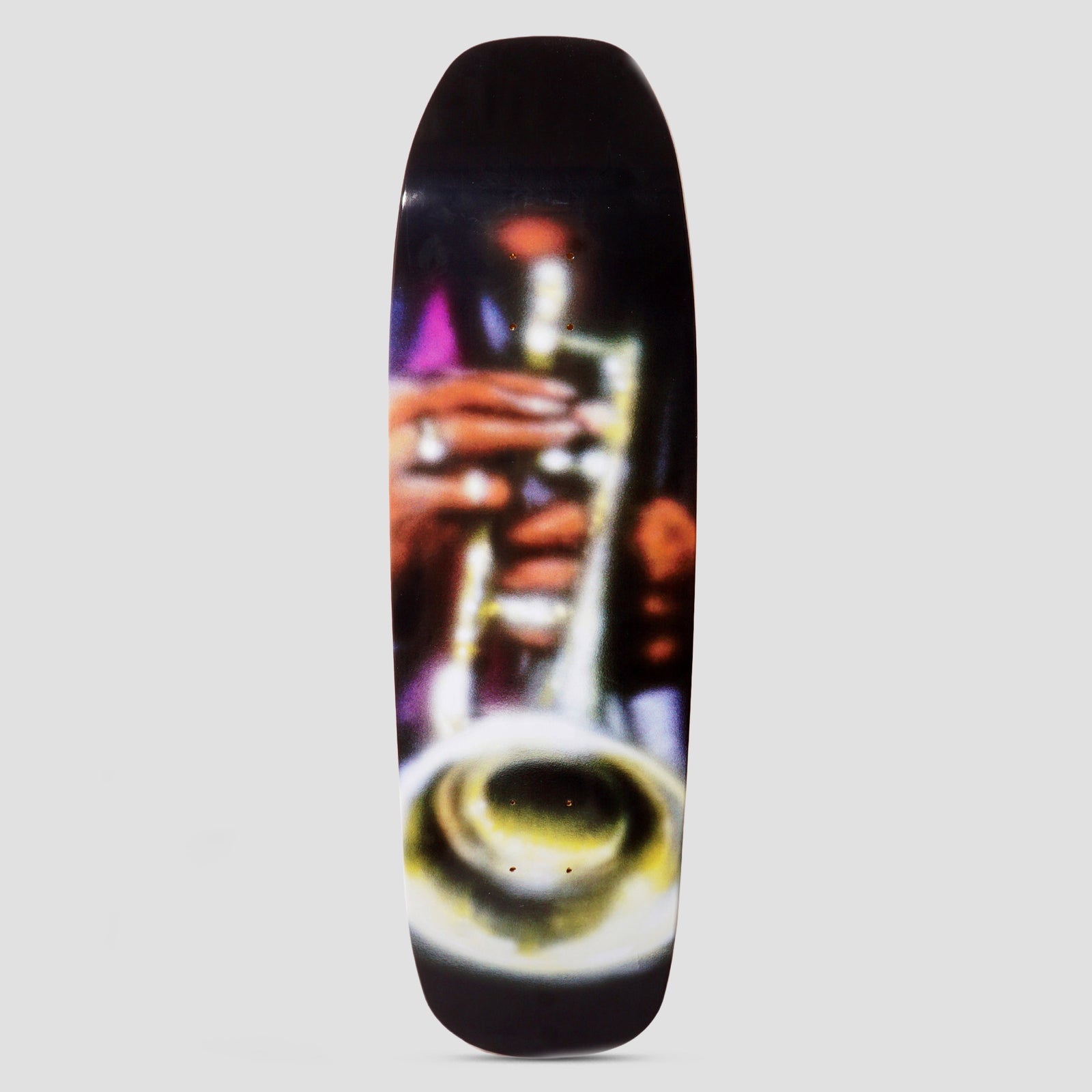 Skateboard Cafe Brass Pub Cruiser skateboard deck: A blurred, soft-focus photographic image of a hand playing a brass trumpet, with the bell in the foreground, on a black shaped cruiser deck.