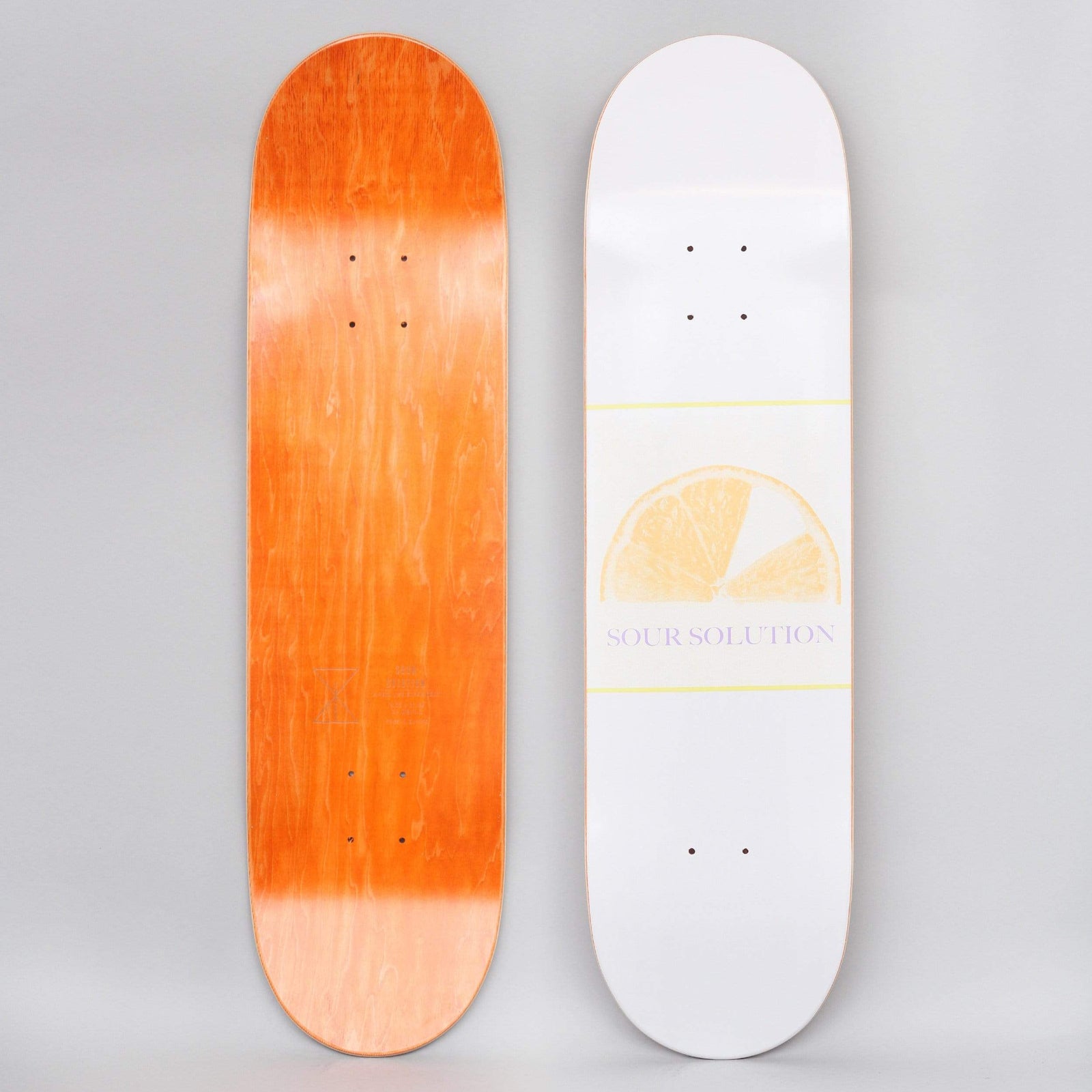 Sour Citrus Grape White skateboard deck: Faded yellow half-slice of citrus fruit between thin yellow lines on a white deck, with SOUR SOLUTION in small lilac serif text beneath. Orange underside shown alongside.