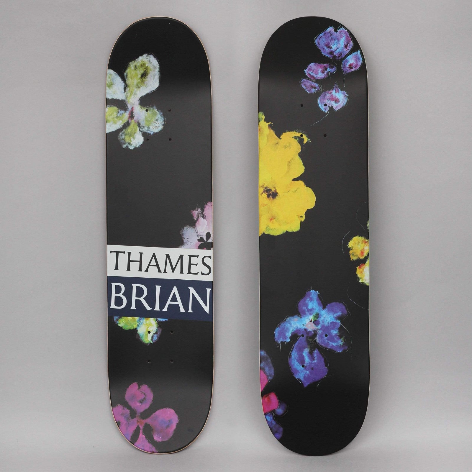 Thames MMXX Thames 7.75 Night Orchid 1 skateboard deck: Loose painted orchid-like flowers in purple, blue, yellow, pink and lime scattered across a black deck. One deck carries a white and navy THAMES BRIAN label across the middle.