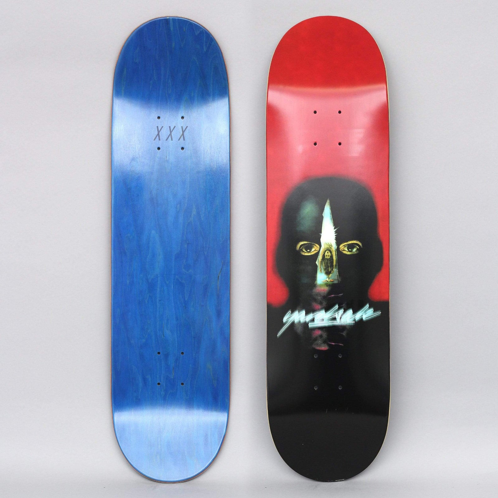 Yardsale Gnar Man Red skateboard deck: A dark airbrushed head with yellow eyes and a pale blade-shaped slit down the face, on a red to black background, with a glowing teal Yardsale script logo below the eyes. Blue underside shown alongside.