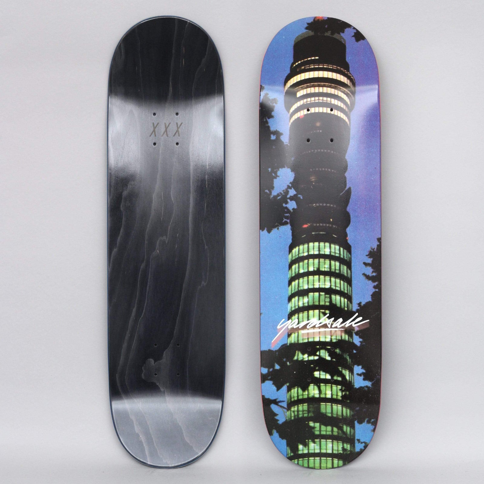 Yardsale BT Tower skateboard deck: Night-time photograph of the BT Tower in London, its lit windows glowing green and yellow, framed by dark tree branches against a blue-purple sky. A white script logo sits across the middle.
