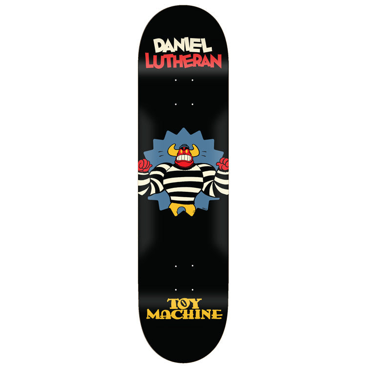 Toy Machine Daniel Lutheran Toons 8.38 skateboard deck: Cartoon horned monster in a black-and-white striped prisoner shirt bursting through a spiky blue wall with red fists raised, on a black deck. Rider name in cream and red at the top and Toy Machine logo in yellow at the bottom.