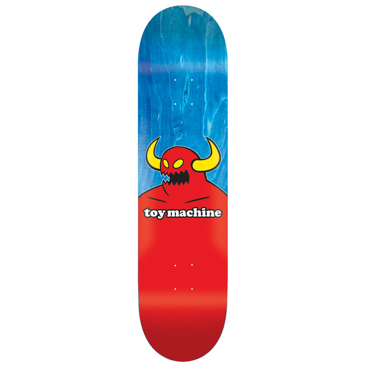 Toy Machine Monster 7.38 skateboard deck: Toy Machine red horned monster with yellow horns and jagged teeth rising from the lower half of the deck, with the brand name on a white label across its chest, over a blue wood-stained upper half.
