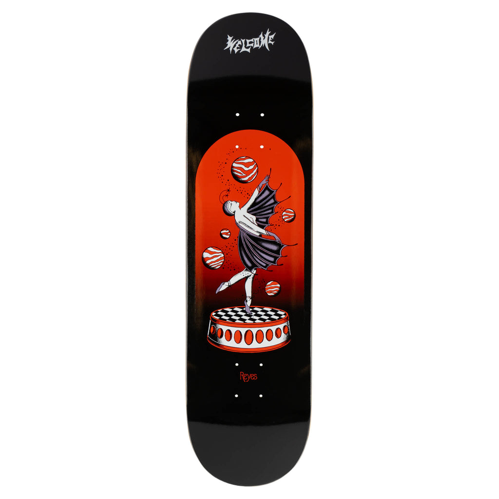 Welcome Ryan Reyes Dancer on Popciscle - Black skateboard deck: A winged dancer in a dark dress balances en pointe on a chequered circular platform, juggling striped red planets inside an arched orange-red panel. Welcome logo at the top on a black deck.