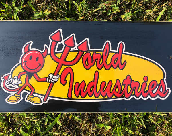 World Industries Devilman Classic Skate skateboard deck: Red smiling devil mascot holding a trident, beside red script World Industries lettering on a yellow oval, on a black deck, with a white sticker-style outline.