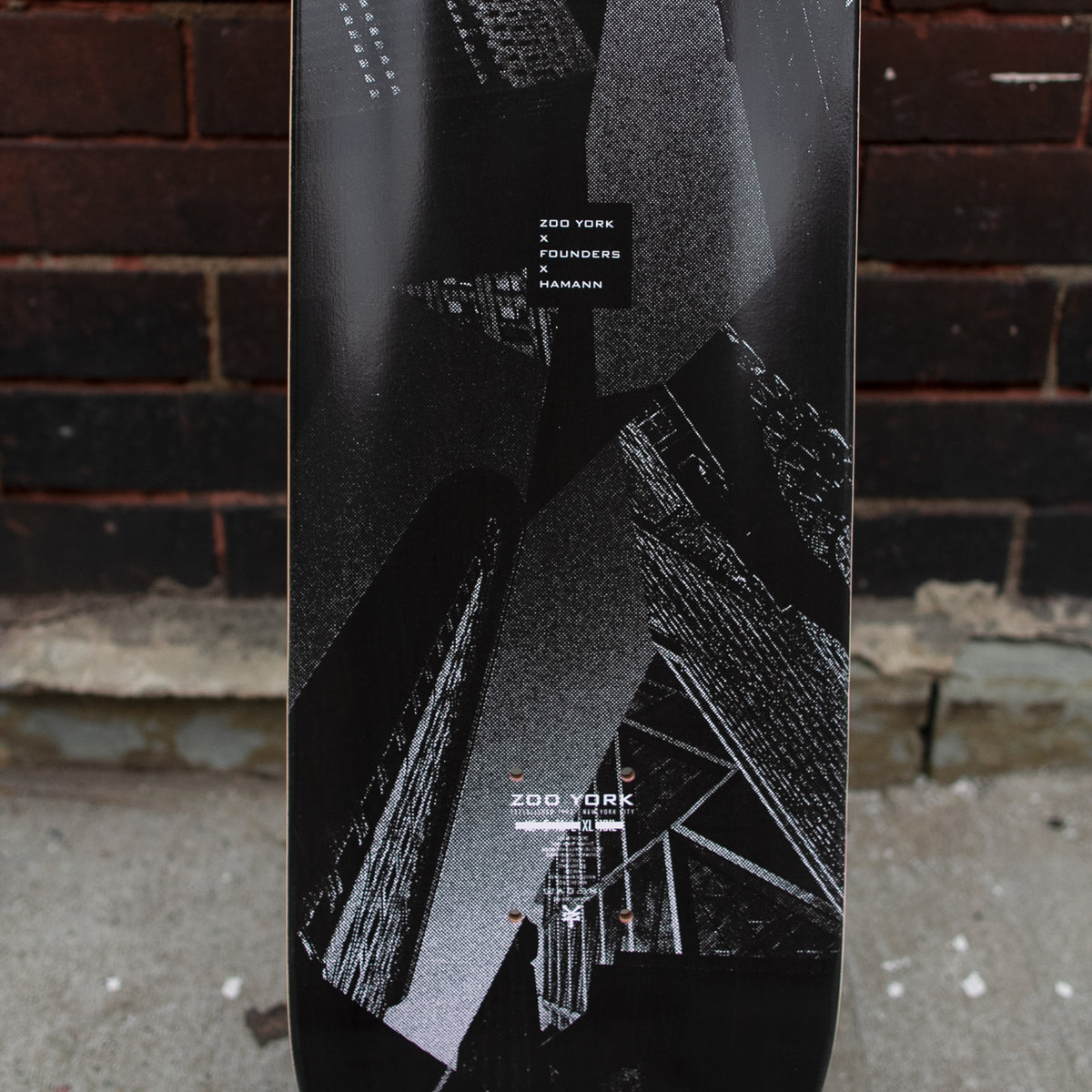 Zoo York Hamann skateboard deck: Black and grey halftone collage of skyscrapers photographed from below, with a small black label at the top naming the collaboration and the Zoo York logo near the tail.