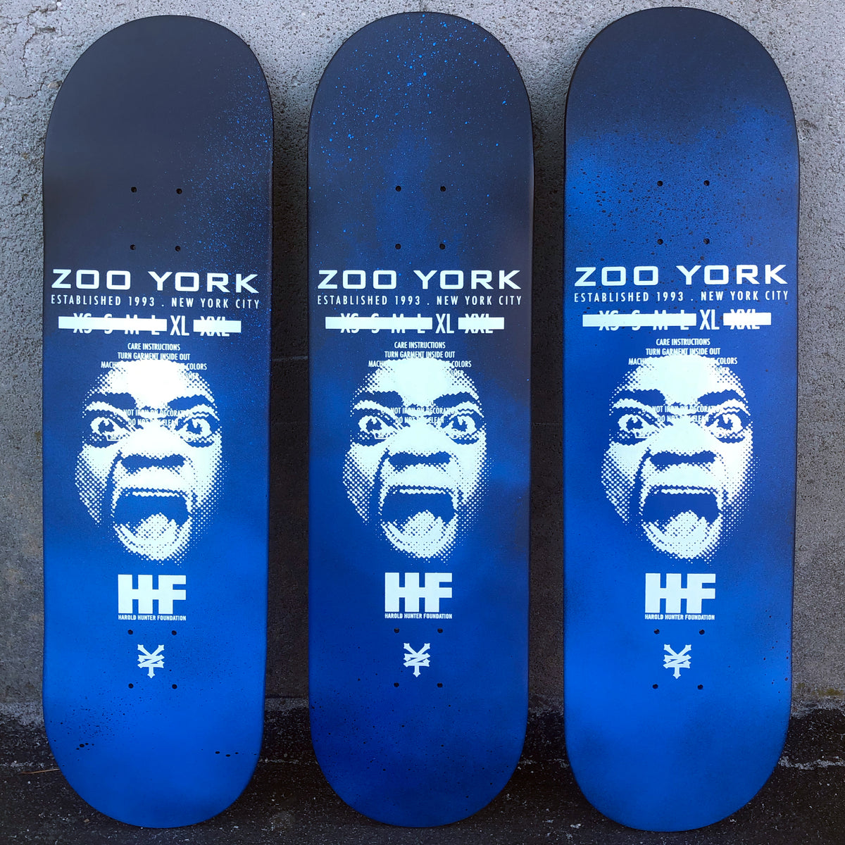 Zoo York Harold Hunter Spray Faded skateboard deck: A halftone white portrait of a screaming face under the Zoo York name and clothing-label style text, above a Harold Hunter Foundation logo and the Zoo York mark, on a black to blue spray-faded ground. Three decks shown with slightly different fades.