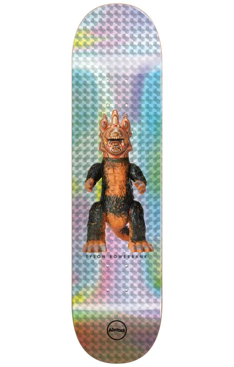 Almost Bowerbank Haroshi Monster Super Sap R7 8.0 & 8.25 skateboard deck: A vinyl toy-style monster with a crested orange head and black and orange furry body stands centred on a holographic silver foil background with a faceted pattern. The rider's name is printed beneath it and the Almost circle logo sits at the tail.