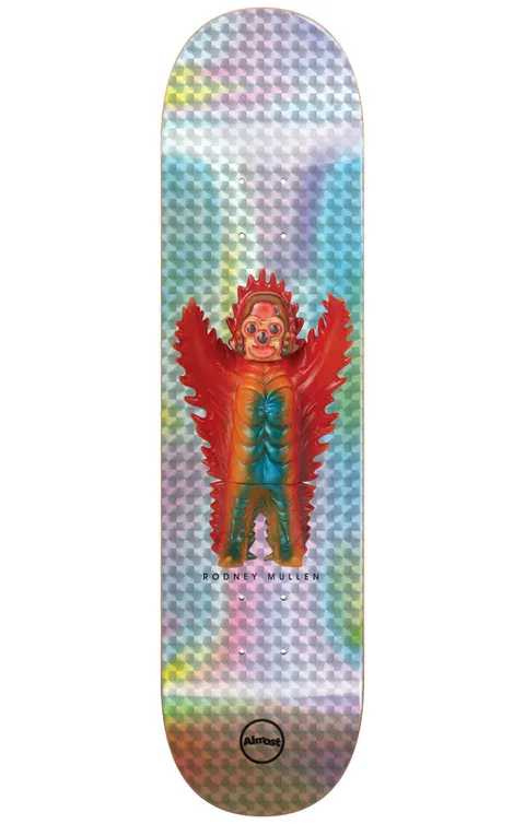 Almost Mullen Haroshi Monster Super Sap R7 7.75 & 8.0 skateboard deck: Photo of a winged red, orange and teal vinyl monster toy with three eyes, standing centrally on a holographic silver foil deck with a chequered pattern.