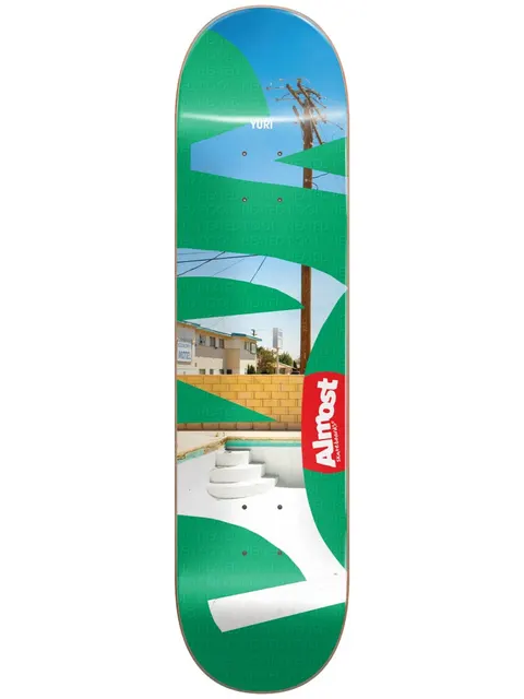 Almost Yuri Fleabag R7 skateboard deck: Photograph of an empty motel swimming pool with white steps, a block wall and a telegraph pole, overlaid with large green leaf shapes and a faint repeated 'heated pool' text. Red Almost logo tag at right.