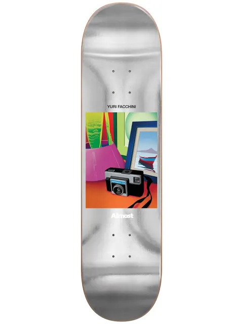 Almost Yuri Life Stills Impact Light 8.375 skateboard deck: Silver foil deck with a small framed illustration in the centre: a vintage instamatic camera on an orange table beside a pink bag, a green plant and a framed picture of a red boat on water.