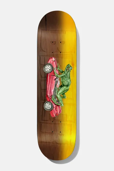 Baker Figgy Dimensions 8.5 skateboard deck: Wood-stained deck fading from brown to yellow-orange, with a faint ghosted Baker logo and a painted green frog pushing a red car along on its side.
