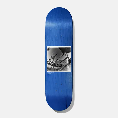 Baker Spanky BAKERVCA 8.25 skateboard deck: Black and white fisheye photograph of a skater mid-trick over a handrail beside a building, set in a white-bordered square on a blue-stained deck, with tiny caption text underneath.