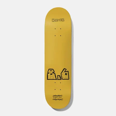 Baker Spanky Mega 8.625 skateboard deck: A plain mustard-yellow deck with the name Kader in small black hand-drawn capitals at the top. Near the tail is a large brick-textured 8.6 in thick black outline, with EIGHT SIX written between barbed-wire scribbles.
