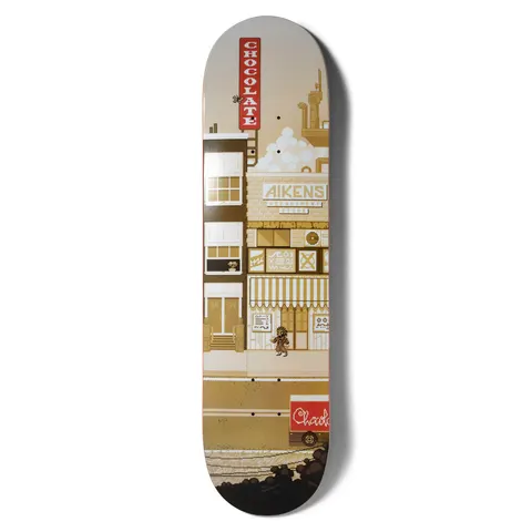 Chocolate Aikens Pixel City skateboard deck: A pixel-art street scene in sepia and cream tones: shopfronts including an Aikens Department Store with striped awning, a small pixel figure walking, a red Chocolate sign and a delivery van with factory chimneys behind.