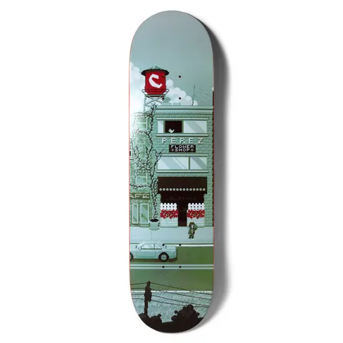 Chocolate Perez Pixel City skateboard deck: Pixel-art street scene in muted greens and grey showing a brick shop front labelled as a flower shop, with a red water tower carrying the Chocolate logo above. A small figure stands outside, with a car and power lines below.