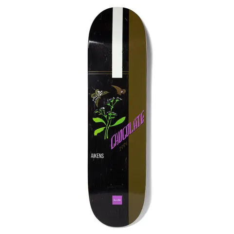 Chocolate Aikens Burn One Pop Secret skateboard deck: Black deck with an olive-brown stripe down the right and a white stripe at the top, with a green plant bearing white flowers and two moths, and Chocolate lettering in purple.