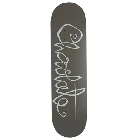 Chocolate Trahan OG Script skateboard deck: Looping, handwritten-style brand script in pale grey running down the length of a plain dark grey deck, with a long underline stroke through the final letters.