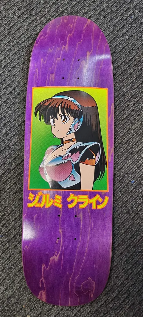JK Industries Dream Girl Purple skateboard deck: An anime-style girl with long dark hair, headband and metallic armour, framed in a green rectangle with an orange border on a purple stained deck. Japanese katakana text beneath in yellow.