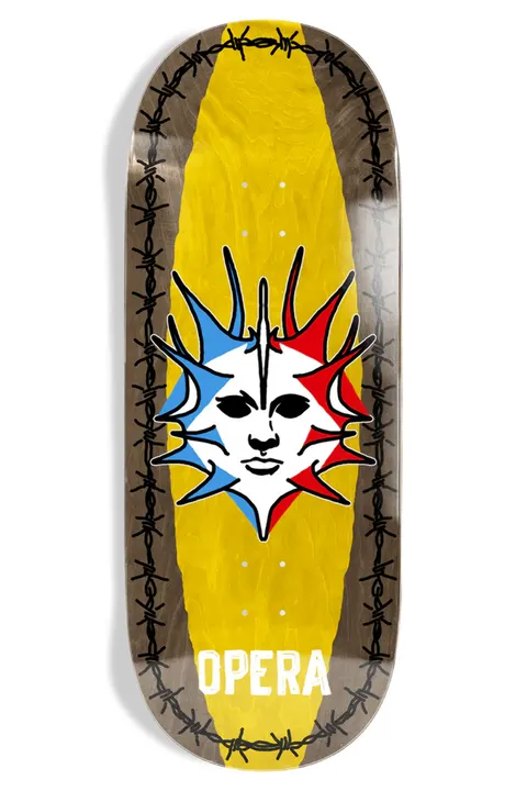 Opera Fatties Torn Spike skateboard deck: Wide, oversized shape with a yellow centre band framed by barbed wire along each edge. A spiky sun-like mask with a blank white face is split into red, white and blue, above the white 'Opera' wordmark.