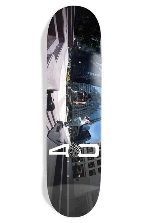 Shut Bryce Kanights Coco & Sheffy EX7 skateboard deck: Full-deck colour photo of two skaters mid-trick between city buildings, shot with a distorted fisheye view and tilted along the deck, with a large white '40' and small crest at the bottom.
