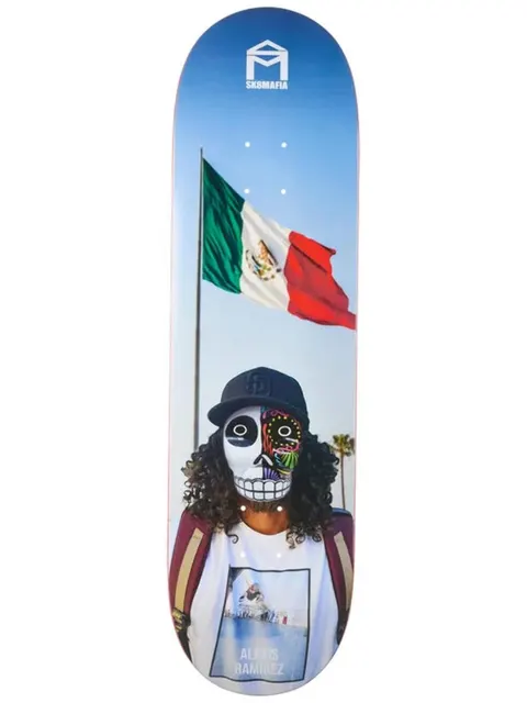 Sk8Mafia Ramirez Dios skateboard deck: Colour photograph of a curly-haired person in a baseball cap and a half-skull Day of the Dead face mask, standing before a waving Mexican flag on a pole against a blue sky. The Sk8Mafia house logo is at the top.