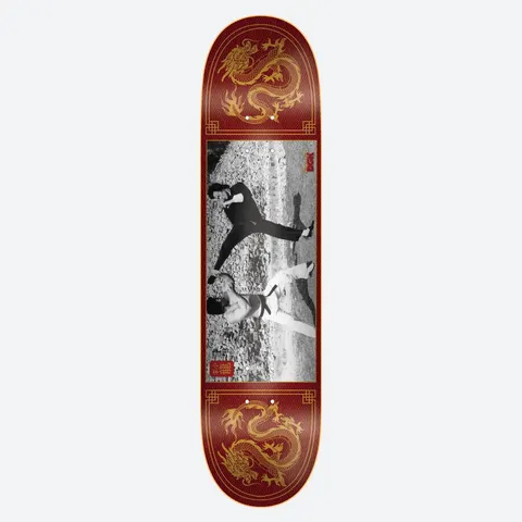 DGK x Bruce Lee Double Dragon skateboard deck: Black and white photograph of two martial artists mid-fight on a rocky ground, set in a red panel with gold Chinese dragons at the top and bottom and a gold border. Small red seal-style logos beside the photo.