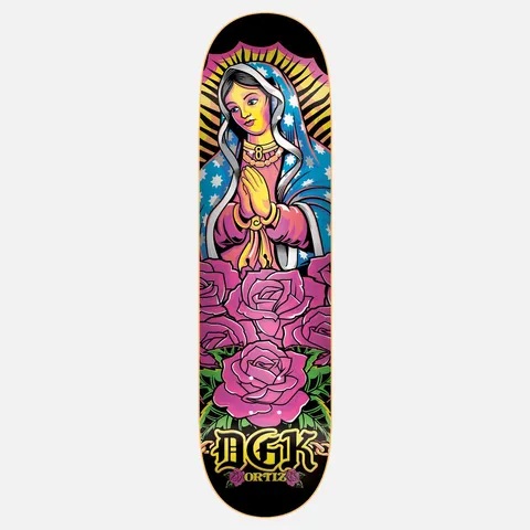 DGK Santa Del Barrio Ortiz 8.1 skateboard deck: Colourful tattoo-style Virgin of Guadalupe with praying hands, starry blue mantle and golden rays, above a bed of pink roses, on black. DGK in gold gothic lettering and ORTIZ at the bottom.