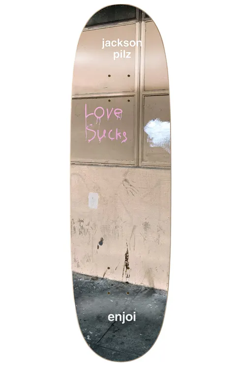 Enjoi Pilz Tweaker R7 8.25 & 9.125 skateboard deck: Photograph of a dirty street wall and pavement with pink graffiti reading 'Love Sucks' on a boarded window. Rider's name at the top and brand name at the tail, in white text on a shaped deck.