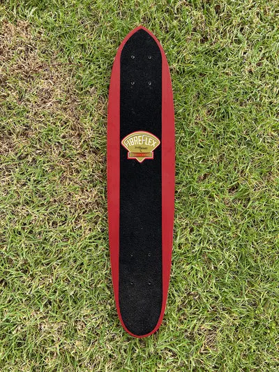 G&S FibreFlex - Slalom Model skateboard deck: Long narrow slalom board with pointed nose and tail, black grip over a red painted edge, and a small gold and red diamond-shaped Fibreflex badge in the centre.
