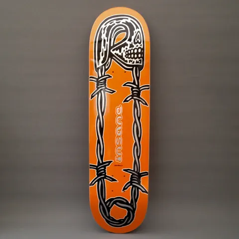 Insane Unsafety Pin skateboard deck: Large safety pin drawn as barbed wire, its head a skull, with black and white outlines on an orange deck. A small grey Insane logo sits in the centre between the wire strands.