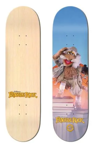 Madrid x Fraggle Rock Traveling Matt 8 skateboard deck: Traveling Matt, a shaggy Fraggle Rock puppet in an explorer's outfit, shades his eyes while standing on a stack of books against a blue and orange sky. Fraggle Rock logo at the bottom; the other deck is plain natural wood with a small logo.
