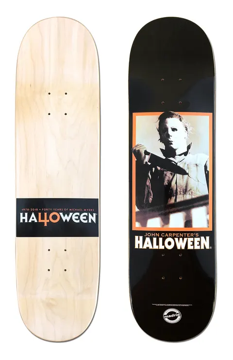 Madrid X Halloween - Stalker 8 skateboard deck: Black deck with a framed film still of a masked figure in a boiler suit holding a knife, in an orange border, above 'John Carpenter's Halloween'. The natural wood underside has a black band reading 'Halloween' with a '40' for the O.