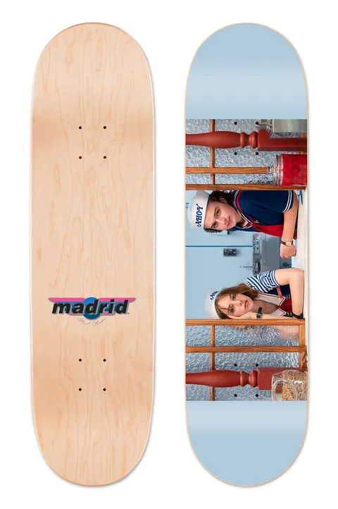Madrid X Stranger Things 3 - Scoops Ahoy 8 skateboard deck: Photographic scene of two people in white sailor caps and navy and white striped uniforms leaning on a soda fountain counter with glass jars, set across a pale blue deck. The natural wood underside has a Madrid logo.