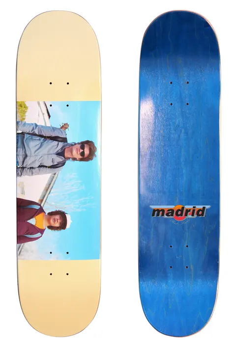 Madrid X Stranger Things - Steve & Dustin 8 skateboard deck: Cream deck with a colour photograph band across the middle showing two characters against a blue sky: a young man in sunglasses and a light jacket, and a boy in a cap and maroon jacket. The underside is blue with a Madrid logo.