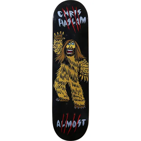 Almost Chris Haslam Hasquatch skateboard deck: A cartoon bigfoot-style creature with a bearded, long-haired human face waves one hand, drawn in bold outlines on a black deck. Red claw slashes cut through the grey rider name at the top and brand name at the bottom.