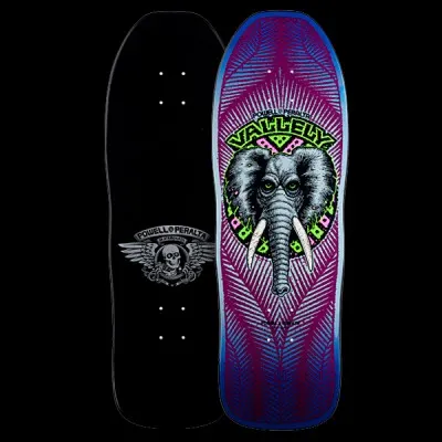 Powell Peralta Vallely Elephant - Purple skateboard deck: Grey elephant head with tusks and green eyes inside a circular green and pink badge, with Vallely lettering above, on a purple deck with blue edges and radiating feather-like lines. Underside shows a winged skull logo. Both sides shown.
