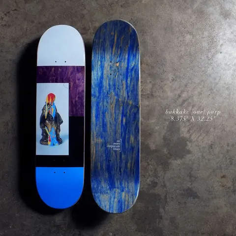 Quasi Bukkake - Purple skateboard deck: Photographic collage: a small bright figurine in a dark robe on a pale panel, framed by purple wood-grain, black and pale grey blocks with a bright blue tail. Bottom face shown beside it with blue stain and a small 'no more corporate blues' mark.