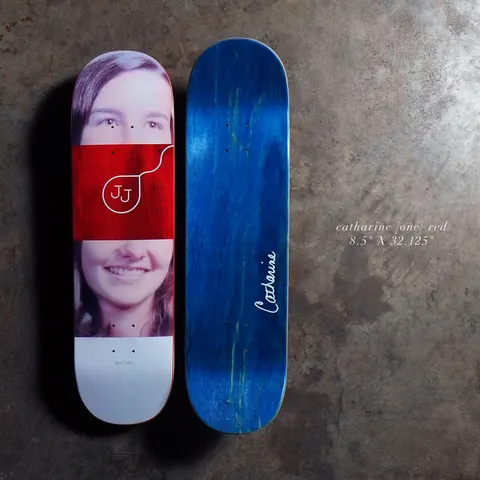 Quasi Catharine - Red skateboard deck: A photographic portrait of a smiling young woman with long hair, split by a red band with a JJ monogram and a looped line. The bottom side is shown in blue stain with a white signature.