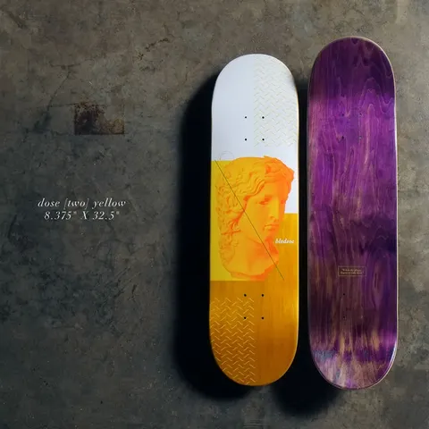 Quasi Dose - Yellow skateboard deck: White and yellow deck with an orange-toned classical marble bust, a diagonal line across it and zig-zag line patterns. Rider name beside the bust; purple stained underside shown alongside.