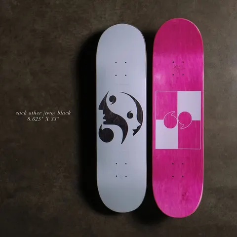 Quasi Each Other - Black skateboard deck: A grey top with an abstract black shape combining a face profile and quotation-mark commas in a yin-yang arrangement. The pink underside shows a quotation mark in a white and pink checked square. Shown as a pair on a dark background.