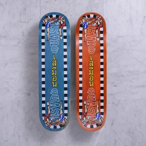 Quasi K.O. Blue skateboard deck: Two Muay Thai fighters kicking at each other in each corner, within a black and white chequered border, with Thai script and outlined QUASI lettering down the board. Shown in blue and orange stains.