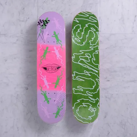 Quasi Lot Lizard Purple skateboard deck: Two decks shown. One has a lilac and pink graphic of green and pale lizards around a drawn mouth with teeth, with a chequered flag at the top. The other is green with a white wobbly outline lettering design.