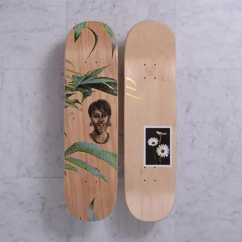 Quasi Mother Natural skateboard deck: Two sides shown on natural wood. One has a pencil-style portrait of a smiling woman among green halftone leaves with gold lettering. The other has a small framed photograph of white daisies on a black background.
