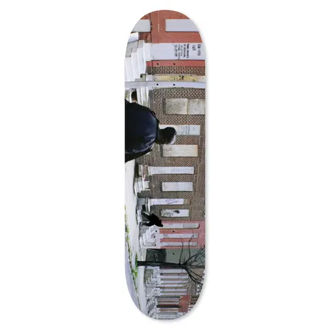 Skateboard Cafe Omar Dom Henry Pro skateboard deck: A full-bleed photograph, turned sideways along the deck, of a man in a dark jacket walking past a row of brick terraced houses with white stone steps. A small black dog and a bare tree are in the lower part.