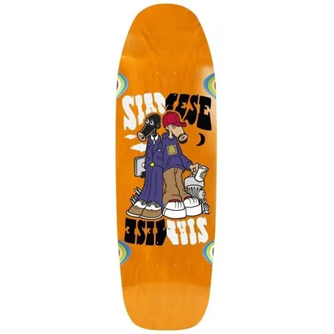 New Deal Siamese skateboard deck: Two cartoon figures standing back to back, one with a black animal head in a purple suit holding a briefcase, the other in a red cap and hoodie holding a cup, under mirrored 'Siamese' lettering. Orange old-school deck with eye shapes at the edges.