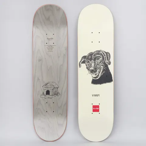Chocolate Vincent Alvarez Big Dawg Cream skateboard deck: Black ink portrait of a smiling dog with floppy ears on a cream deck, with a name below and a small red brand square at the tail. The underside shows a doghouse drawing on grey stain.